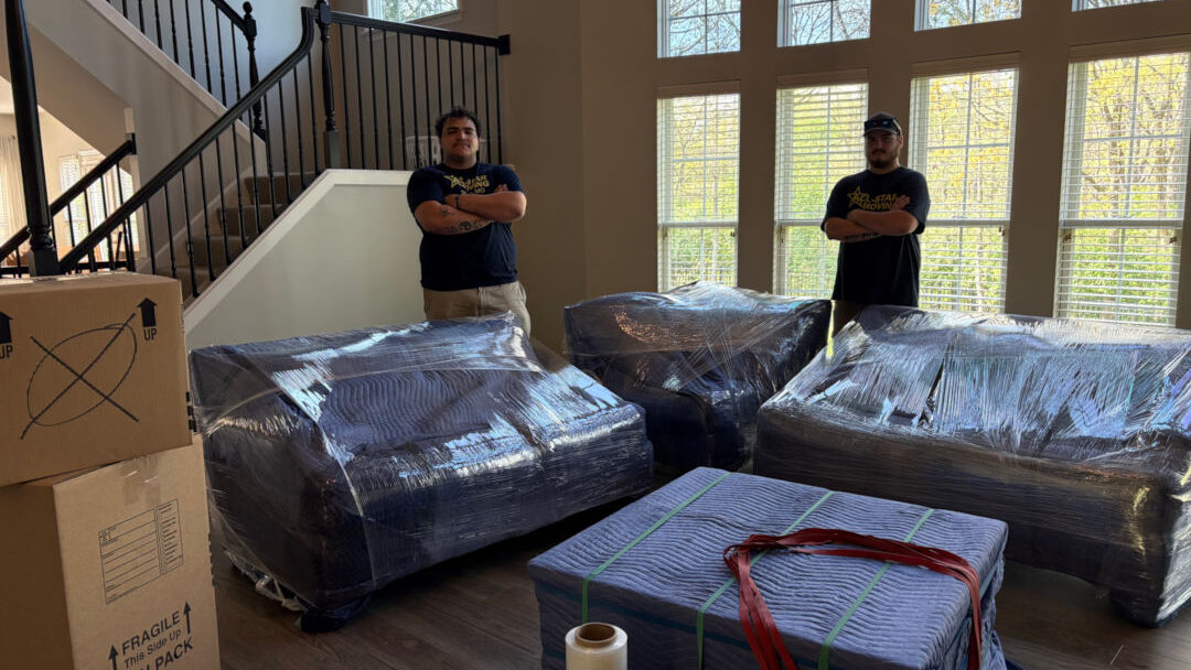 two movers posing next to furniture ready to be moved.